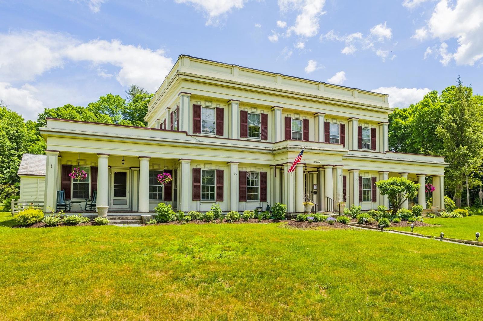 The white clapboard Main House of The Arlington Inn with red shutters, summer sky